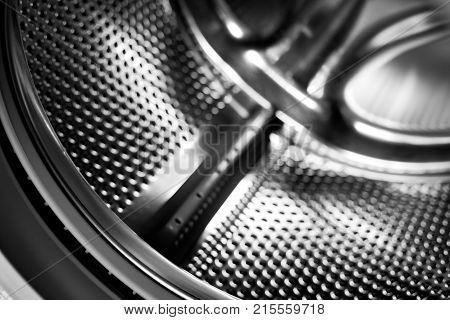 Washing machine drum interior. Perforated stainless steel drum for automatic washing machine. Black and white, metallic background