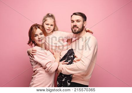 Happy young family with one little daughter posing together on pink studio background