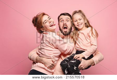 Happy young family with one little daughter posing together on pink studio background