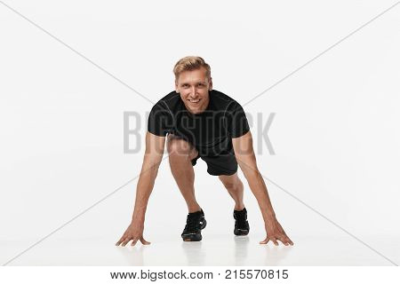 Handsome young man standing in crouch start ready to run while posing at camera on white.