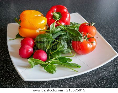 Fresh green vegetable salad with radish tomatoes color peppers on the white plate