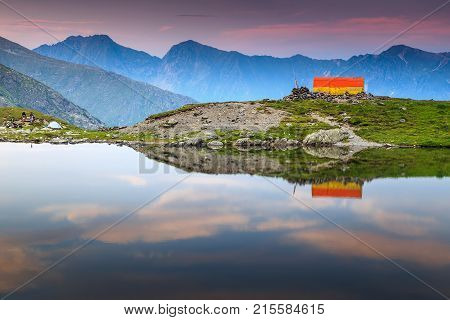 The beautiful alpine Caltun lake and colorful mountain shelter with stunning sunset, Fagaras mountains, Carpathians, Transylvania, Romania, Europe