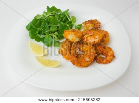 Fried shrimps on a plate. Prawns fried in breading on a white plate with salad and lemon.