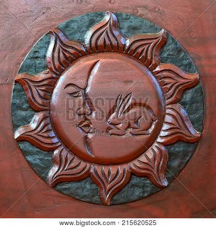 Close up sun with face and hare carved on dark wood used for interior decoration
