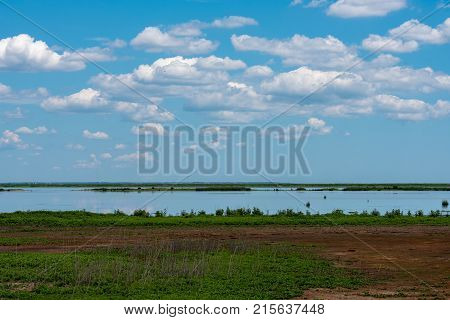 Puffy Wwite clouds in a blue sky hover over Marshlands with deep green grasses