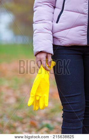 Close-up of a girl in an autumn park, outdoors, stands with rubber, yellow gloves in her hands, to harvest the fallen leaves.