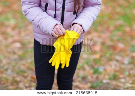 Close-up of a girl in a pink jacket dresses yellow gloves, for cleaning in an autumn park.