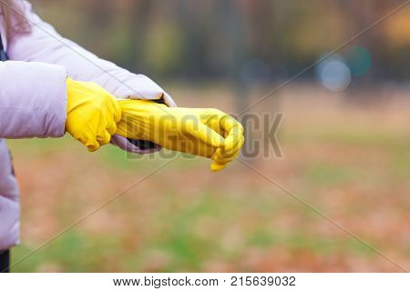 Close-up of a girl in a pink jacket dresses yellow gloves, for cleaning in an autumn park.