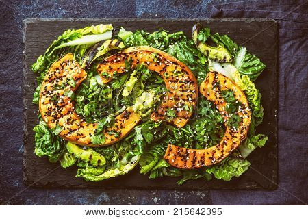 Grilled pumpkin and lettuche salad with white and black sesame and balsamic sauce on slate black board, blue stone background