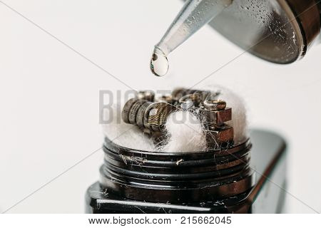 Rebuildable dripping atomizer or RDA for vaping or e-cigarette with Alien Clapton coil and cotton stripes wetted with e-liquid, modern vape device for quit smoking, macro photo with selective focus