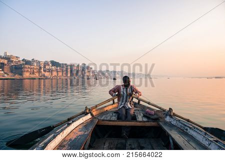 VARANASI INDIA - MARCH 15 2016: Horizontal picture of indian oarsman at the boat at the sunrise in Ganges River in Varanasi India.