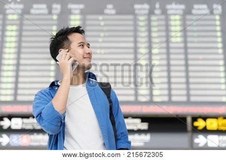 Asian man student use mobile phone and looking out to copy space at right handside with table time at terminal airport. Travel and technology concept.