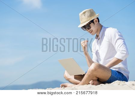 Smart asian man and laptop with cheerful and success posing on beach and blue sky background.Vacation and work concept.
