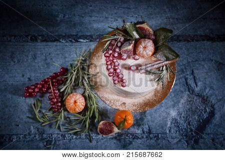 Top view of white christmas cake decorated with red berries tangerin figs and rosemary on wooden background