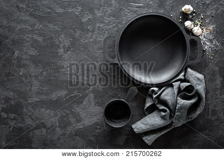 Empty cast-iron pan with cutlery on dark background for restaurant menu top view