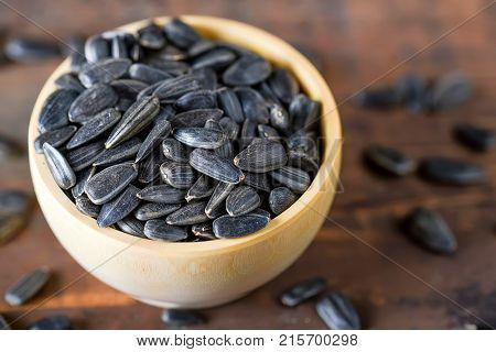 Close up unpeeled sunflower seeds in wooden bowl on dark wooden table