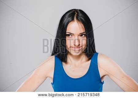young thoughtfull woman with long brunette hair in blue dress in photostudio on gray background