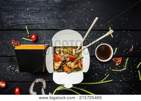 Wok. Udon Stir Fry Noodles With Seafood In A Box On Black Background. With Chopsticks And Sauce.