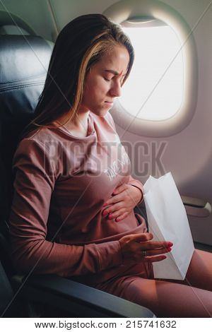Girl is sick in the airplane and seating with paper pocket