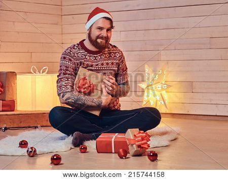 Redhead bearded male in Santa hat in a room with Christmas decoration.
