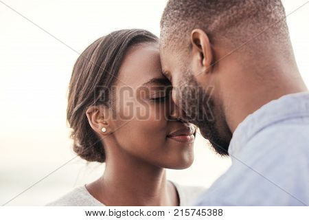 Content young African couple smiling and standing face to face while enjoying a late afternoon sunset together at the beach