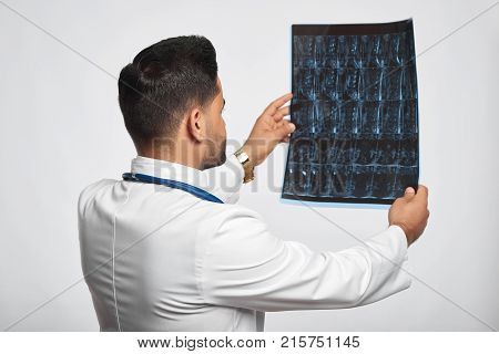 Rearview shot of a male doctor in white labcoat examining an x-ray or MRI scan on gre background at studio profession occupation job experience trustworthy medicine research health people.