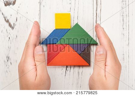 hands surround a wooden house made by tangram home insurance concept or representing home ownership