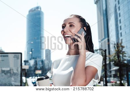 Graet business news from coworker. Beautiful young businesswoman looking away with smile while
talking on mobile phone outdoors