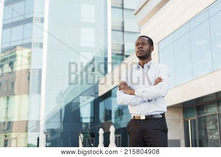 Portrait of thougtful confident black businessman against modern glass office center background. Pensive young african-american executive outdoors.