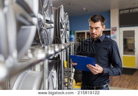 business, maintenance and people concept - male manager with alloy wheel rims and clipboard at car repair service or auto store