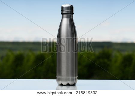 Stainless thermos, water bottle on the sky and forest background