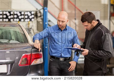 auto service, repair, maintenance and people concept - mechanic with clipboard and customer or car owner looking at taillight at workshop