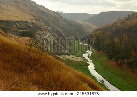 Beautiful landscape of the autumn forest in rainy day. Between the mountains a small river flows. Moldova, Edinet