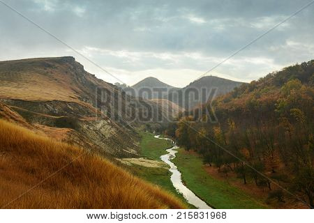 Beautiful landscape of the autumn forest in rainy day. Between the mountains a small river flows. Moldova, Edinet