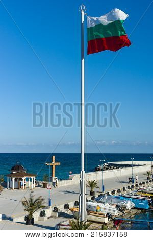 POMORIE BULGARIA - AUGUST 26 2017: Chapel of St. Nicholas in the sea port of the seaside resort town of Pomorie and the national flag of Bulgaria in the foreground.