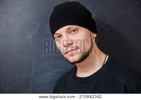 young bearded attractive man in black with a confident look on the background of a school board