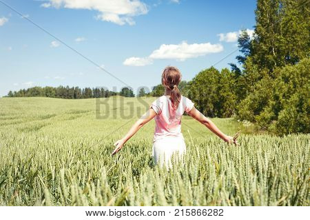 Young cheerful teenage girl with her face upward and opened outstretched arms enjoying the spring sunlight in green wheat field. Multicolored vibrant outdoors horizontal image with vintage filter.