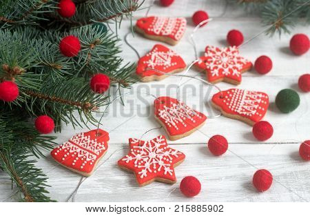 Gingerbread bells and stars, a garland of felted beads and fir branches on a light background - a Christmas or New Year's card. Selective focus.