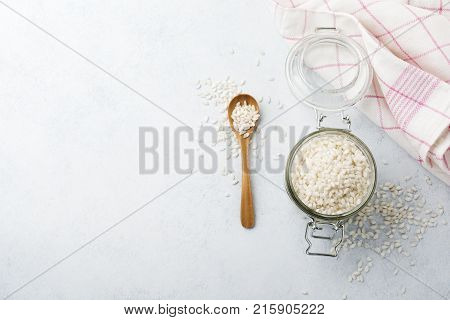 Raw White rice variety Arborio for Italian risotto dishes in glass jar on white concrete or stone background. Selective focus. Top view. Copy space.