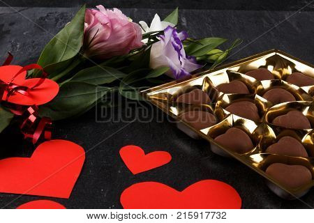 A bouquet of Japanese roses tied with a ribbon with a heart with a box of chocolate. Carved hearts of sweets close-up on a stone background