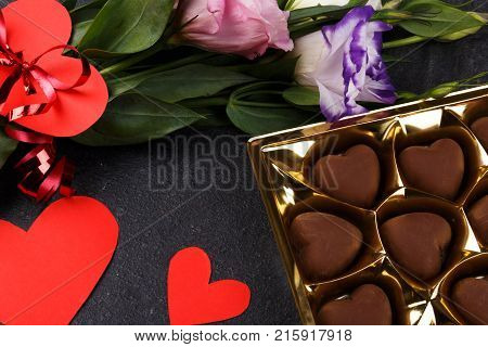A bouquet of Japanese roses bandaged with a ribbon with a heart with a box of chocolates. Carved hearts are shown not completely on a stone background