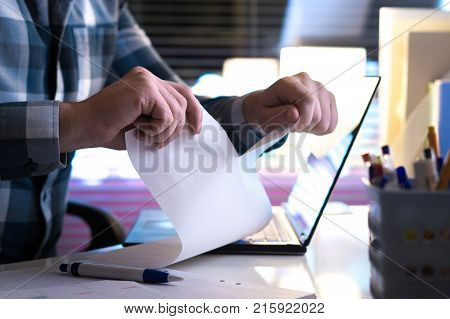 Angry man tearing paper in half home or in modern office at night. Ripped document contract or bill. Business person with company bankruptcy.