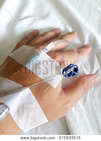 Patient hand with the tube of normal saline infusion on white cloth background