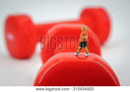 Sport and fitness concept. Man runner miniature figure running on red 1kg dumbbell