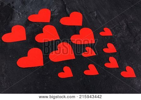 Red hearts of different sizes go from the smaller to the larger are directed to the left close-up on a stone background
