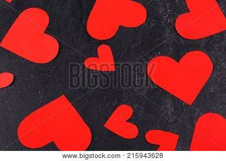 Red hearts of different sizes are scattered close-up on a stone background