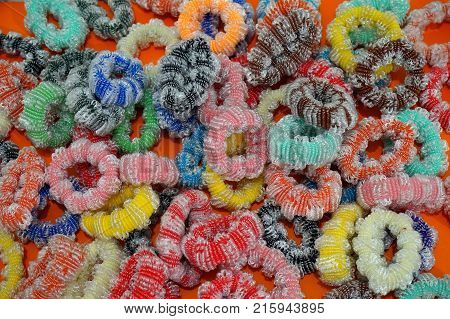 Multicolored eraser for styling hair. Contoured colors. Blue black green pink yellow brown. All colors. Beauty. The white spiral thread runs along the entire elastic band. Red background. Multi-colored photo.