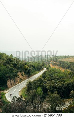 Silhouette of cyclist climbs long mountain road alone solitude through green trees early fall weather and sunlight warming the day shot from above with landscape views