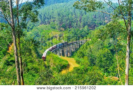 The train running along the Nine Arches Bridge is seen through the jungle gadens and farms from the mountain located in valley Demodara Ella Sri Lanka.