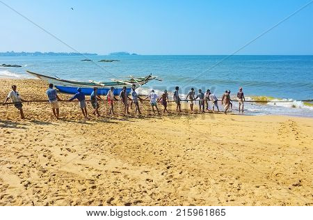 BENTOTA SRI LANKA - DECEMBER 6 2016: The crew of fishermen manually pulls their net out of the ocean standing on the fine sand beach on December 6 in Bentota.